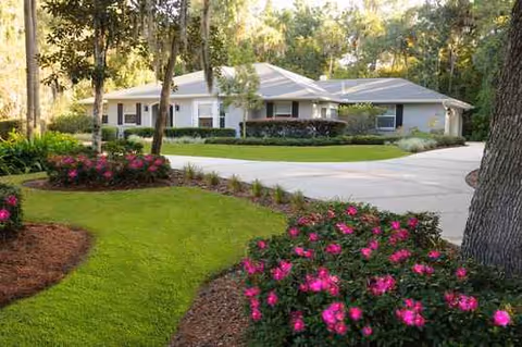 A single-story assisted living facility with manicured lawn and blooming pink flowers.