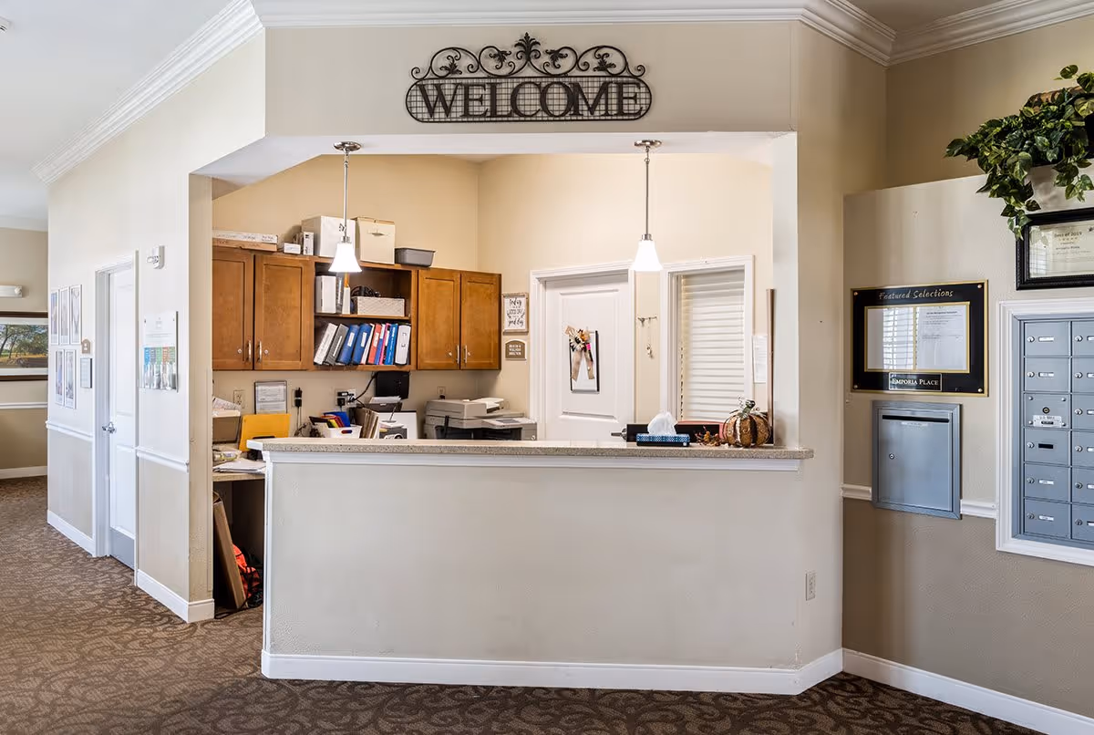 Reception desk and office area with a 'WELCOME' sign overhead, cabinets, mailboxes, and decorative plants.
