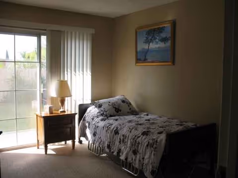 Single bed with floral bedspread beside a nightstand and sliding glass door in a bedroom.