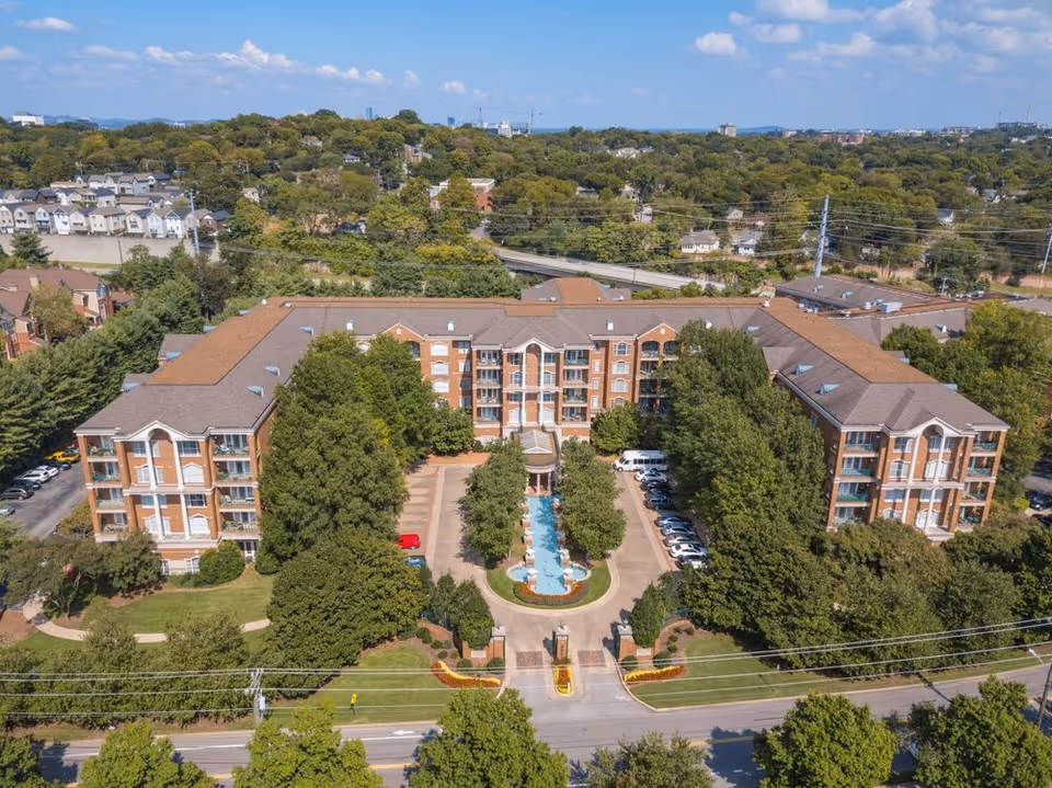 Aerial view of the Richland Place brick apartment-style senior living building with a central fountain, landscaped trees, and surrounding parking.