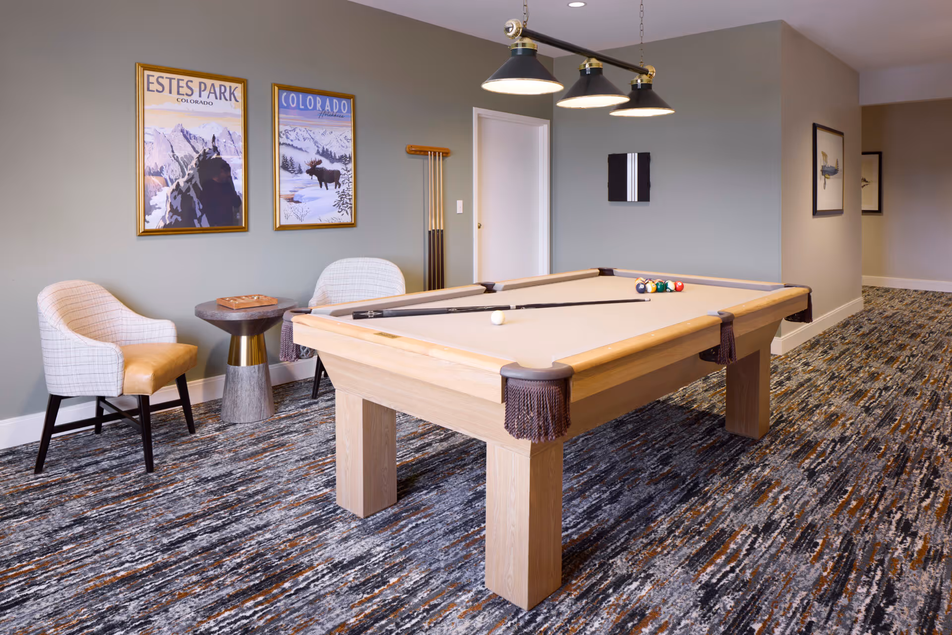 Well-lit interior recreation room featuring a pool table, two chairs, side table, and framed Colorado posters on the wall.