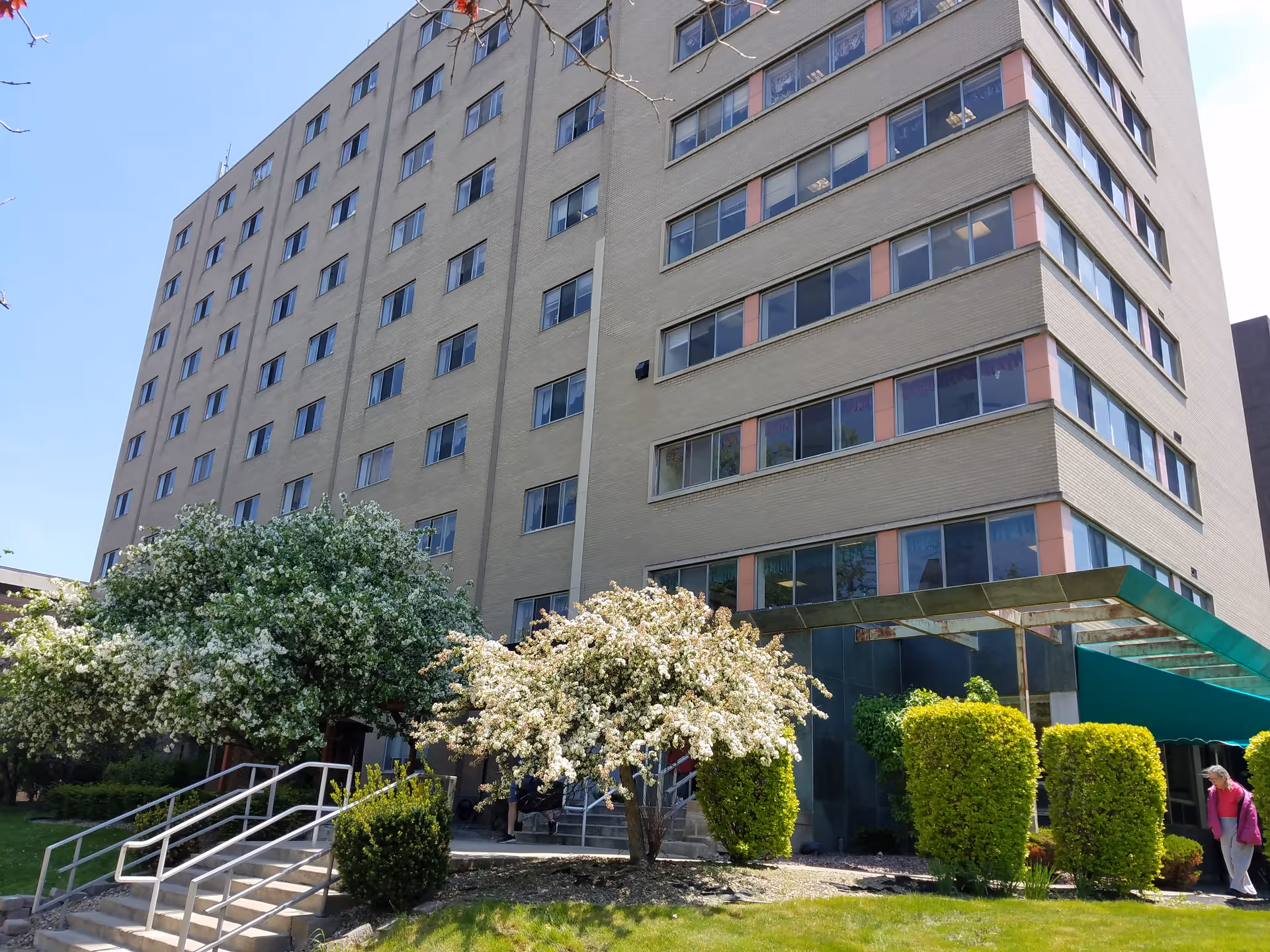 Exterior view of a multi-story senior living building with an entrance, flowering trees, and landscaped shrubs.