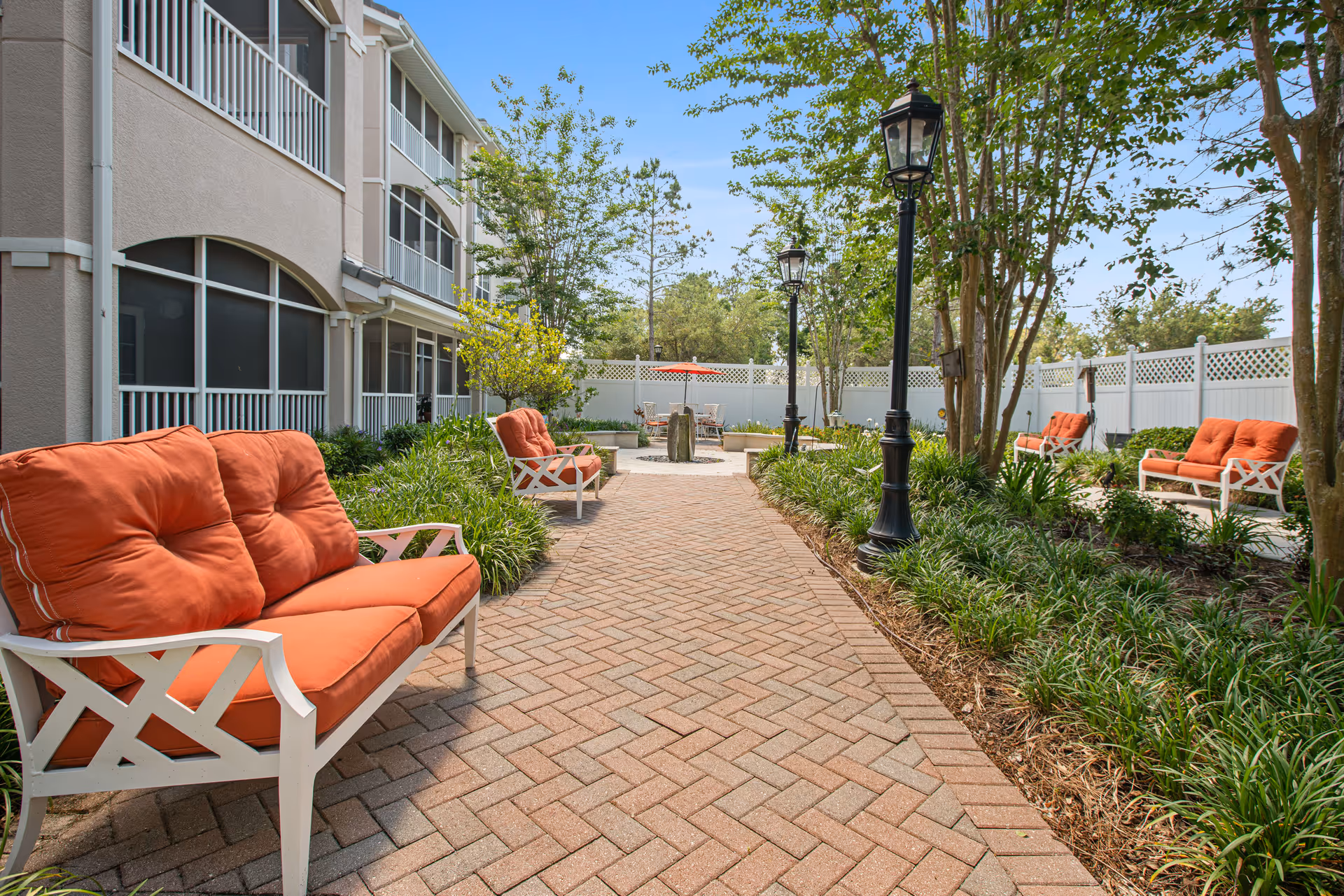 Paved courtyard with orange-cushioned benches, lampposts, and landscaping between residential buildings.