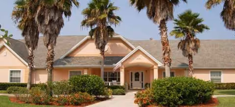 Front view of a pink Brookdale senior living building with palm trees and landscaping.