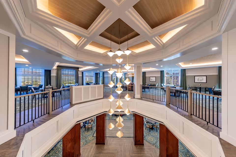 Two-level elegant interior common area with a central hanging chandelier, balcony railings, and seating/dining areas under a coffered ceiling.