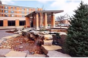 Entrance of a multi-story brick senior living building with a covered porte-cochère and a landscaped stone water feature in front.