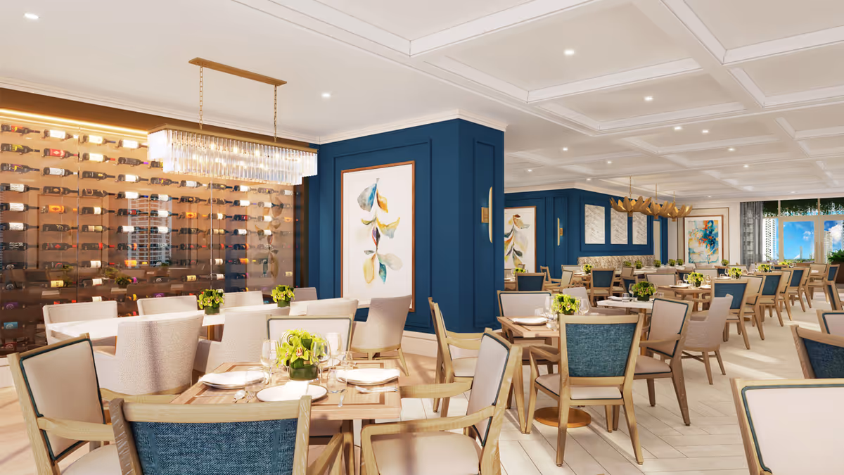 A spacious and elegant dining room with multiple wooden tables and cushioned chairs arranged neatly. The room features blue accent walls adorned with framed artwork, a modern chandelier, and a large glass wine display wall. The space is well-lit with recessed ceiling lights and has large windows offering a view of the cityscape outside.