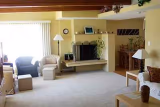 A sunlit senior living room with sofas, tables, and a fireplace in a spacious lounge.