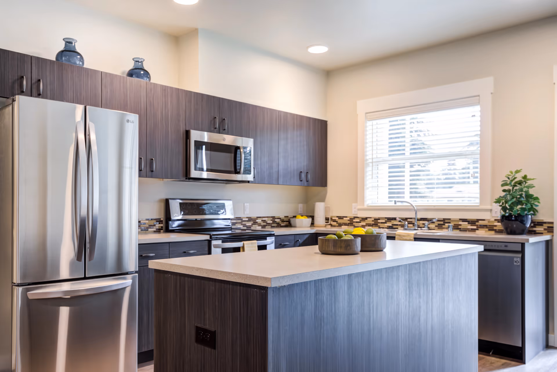 Modern kitchen with a central island, stainless steel appliances, dark wood cabinets, and a window over the sink.