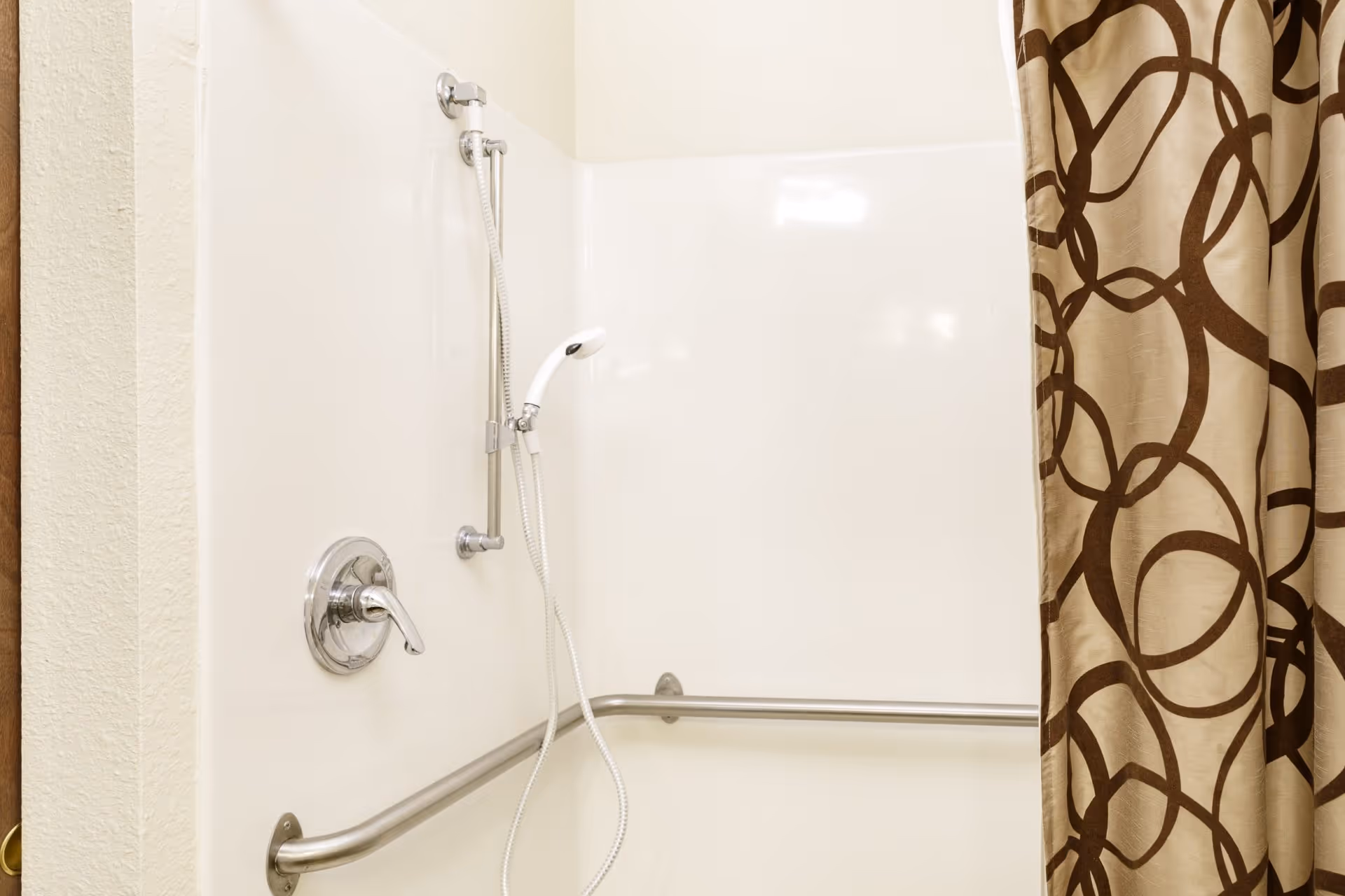 Shower stall with a handheld showerhead, horizontal grab bar, and a patterned shower curtain.