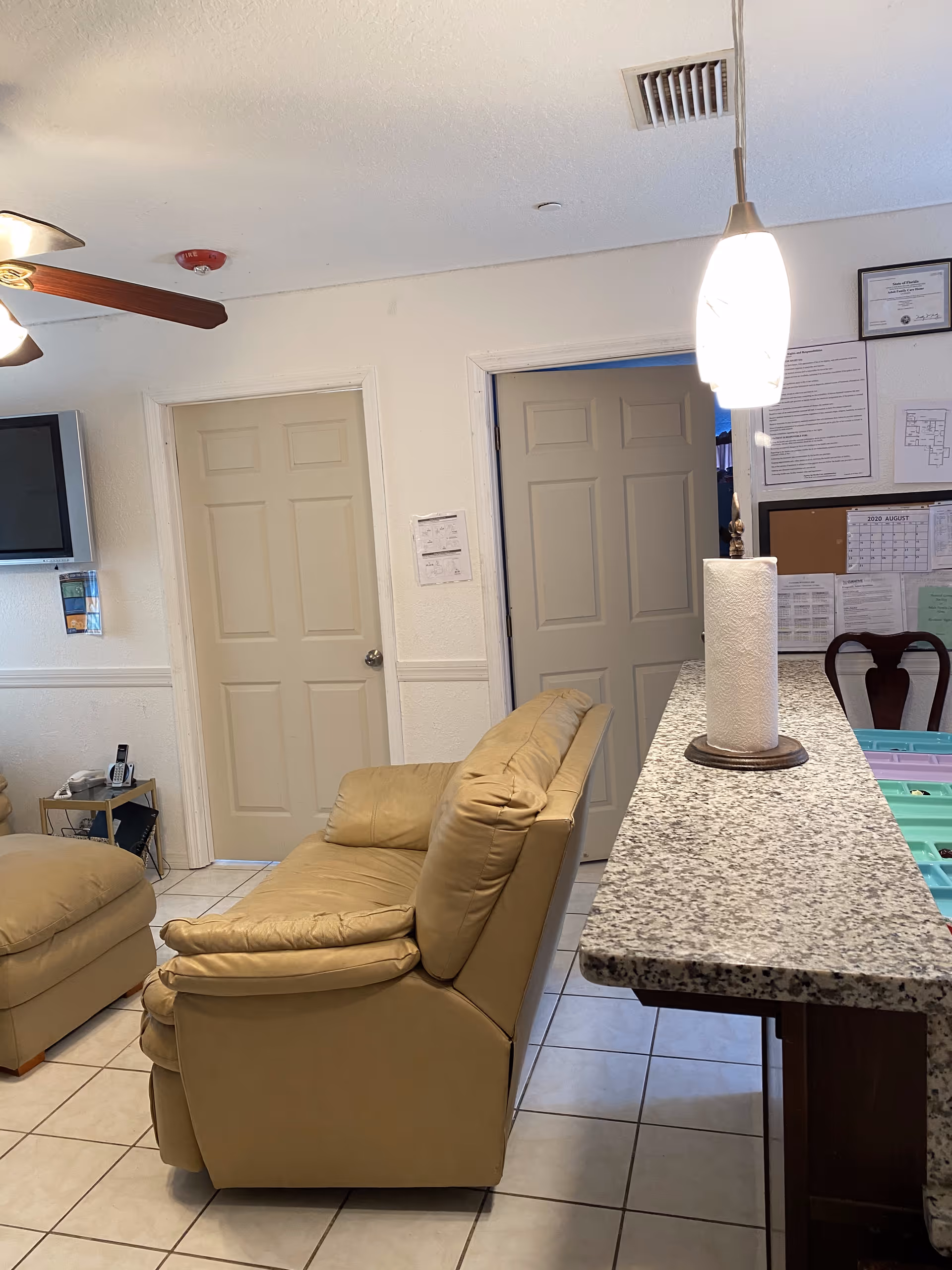 Small living area with a tan leather loveseat and ottoman near a granite countertop topped by a pendant light and paper towel roll.