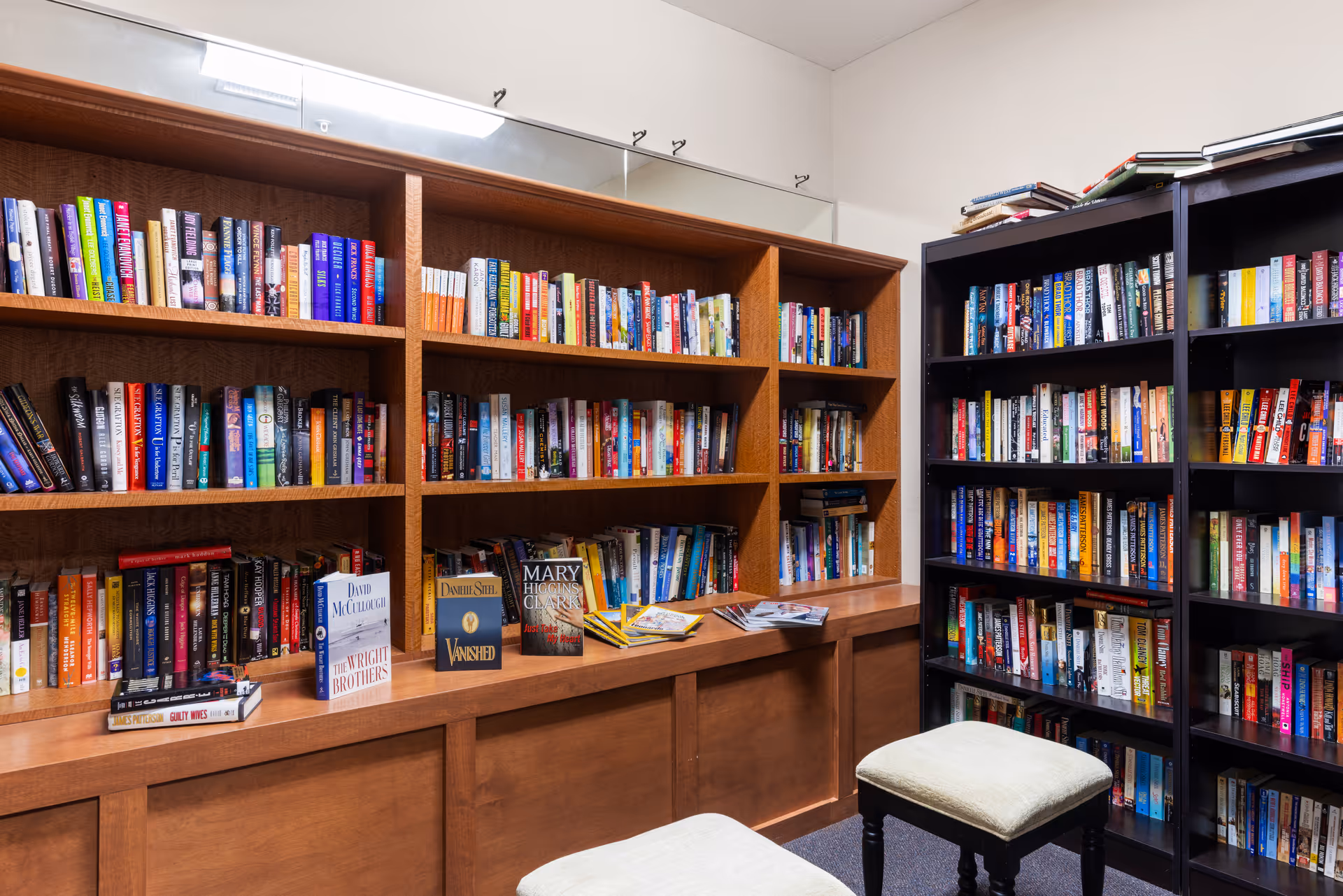 Small library room with wooden bookshelves filled with books and two upholstered stools.