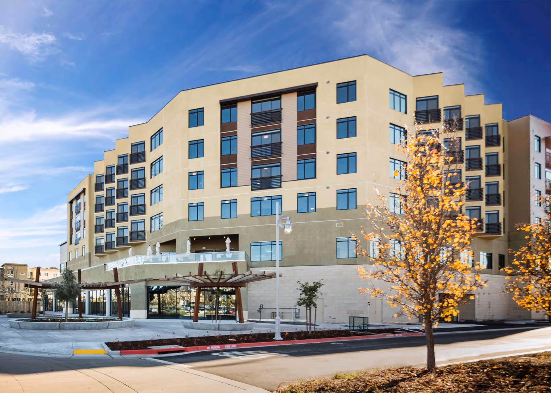 Front exterior of a multi-story senior living building with a driveway, landscaping, and trees.