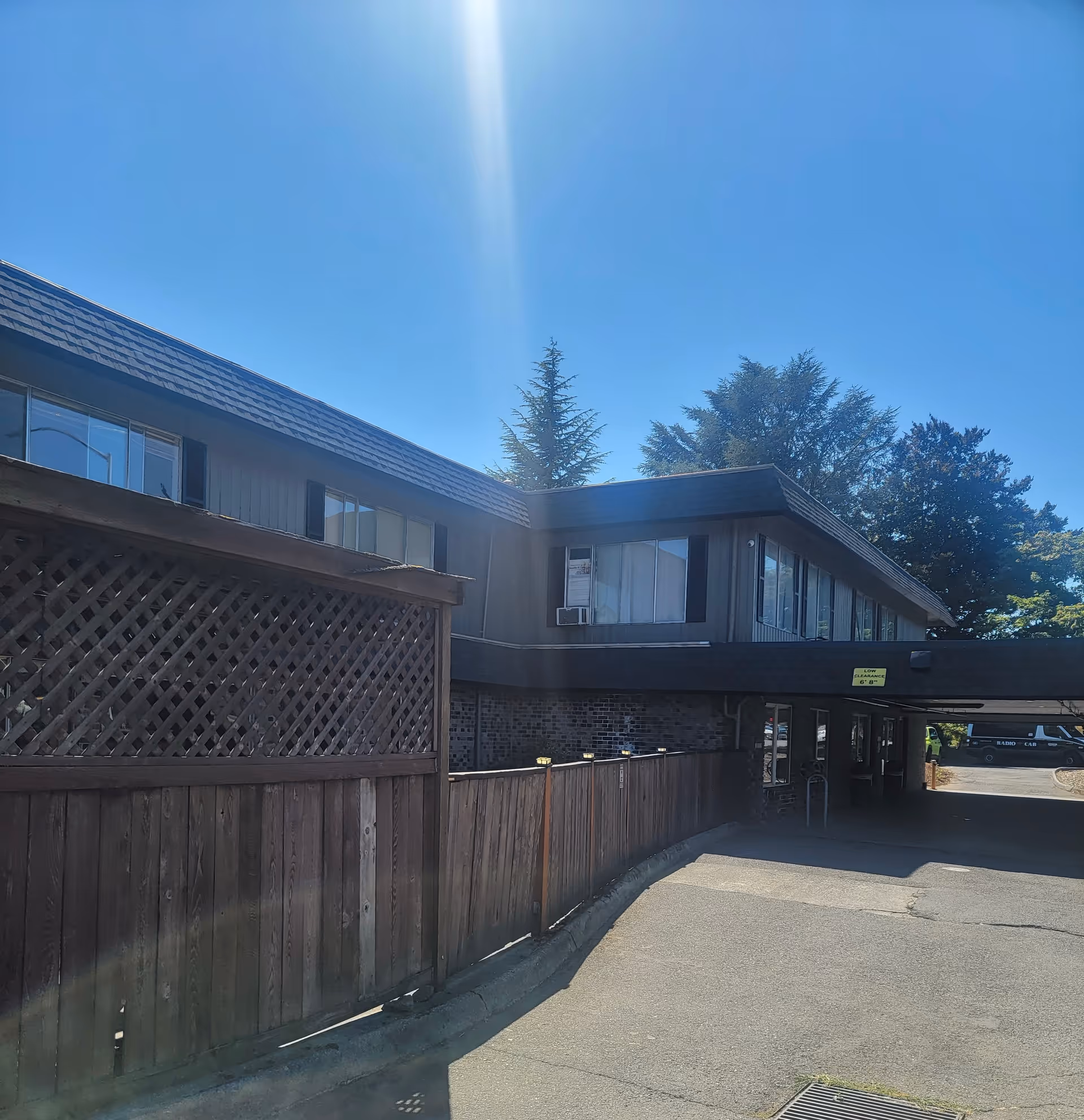 Two-story building exterior with a wooden fence and a covered drive-up entrance under a clear blue sky.