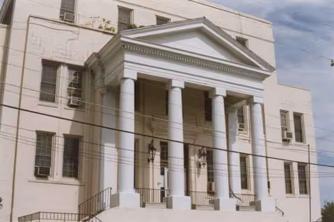 White neoclassical entrance with tall columns and a triangular pediment at a building front.
