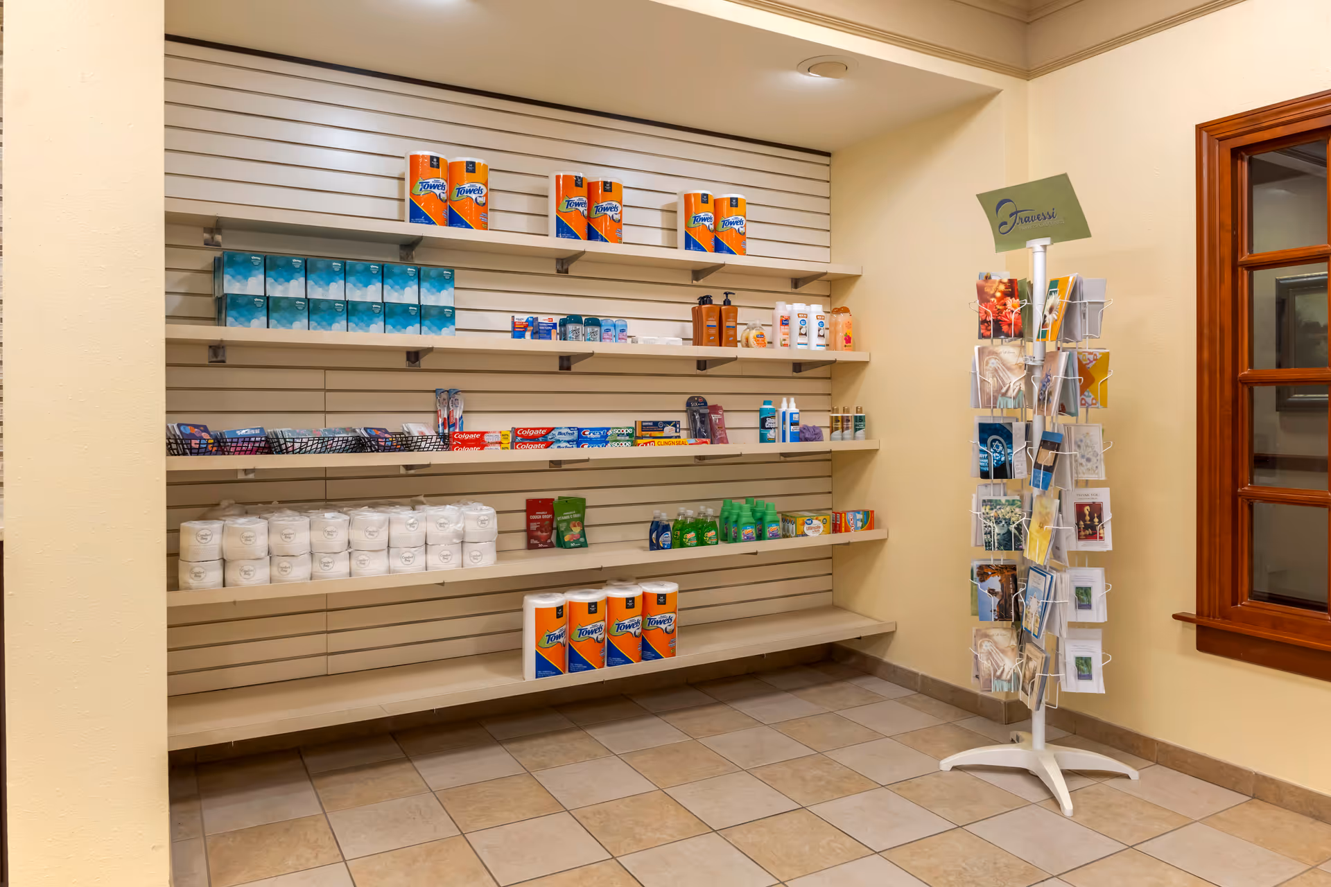 Small interior shop area with shelves stocked with toiletries, paper towels and a rotating greeting card rack.
