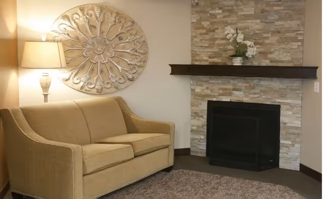 Cozy sitting area with a beige loveseat, lamp, decorative wall medallion, and a stone fireplace with a mantel.