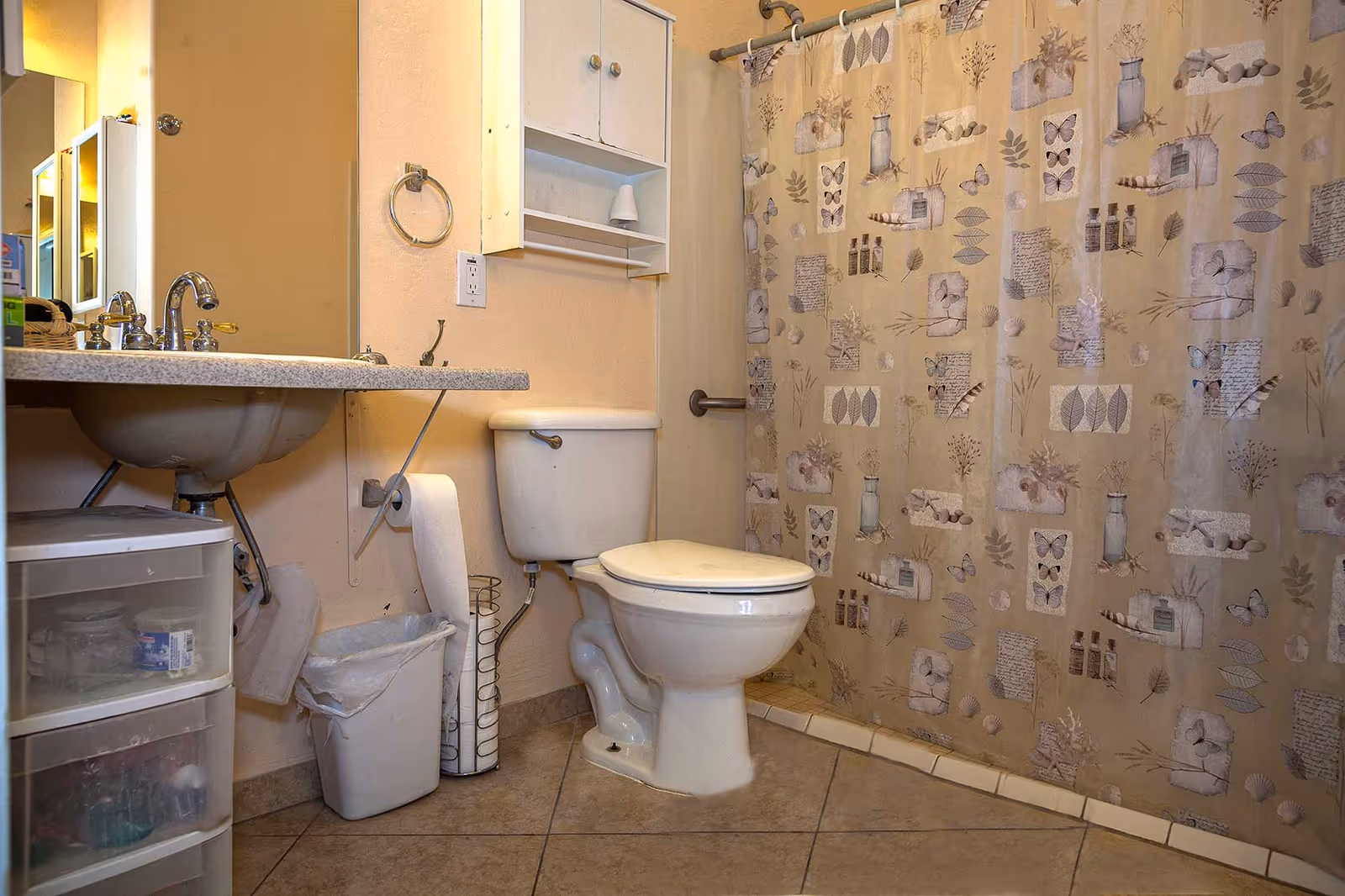 Small bathroom with a toilet, sink with vanity, plastic storage drawers and a patterned shower curtain.