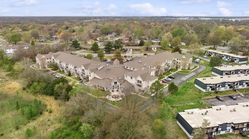 Aerial view of College View Manor, a large senior living facility surrounded by trees and greenery, with multiple connected buildings and parking areas visible.