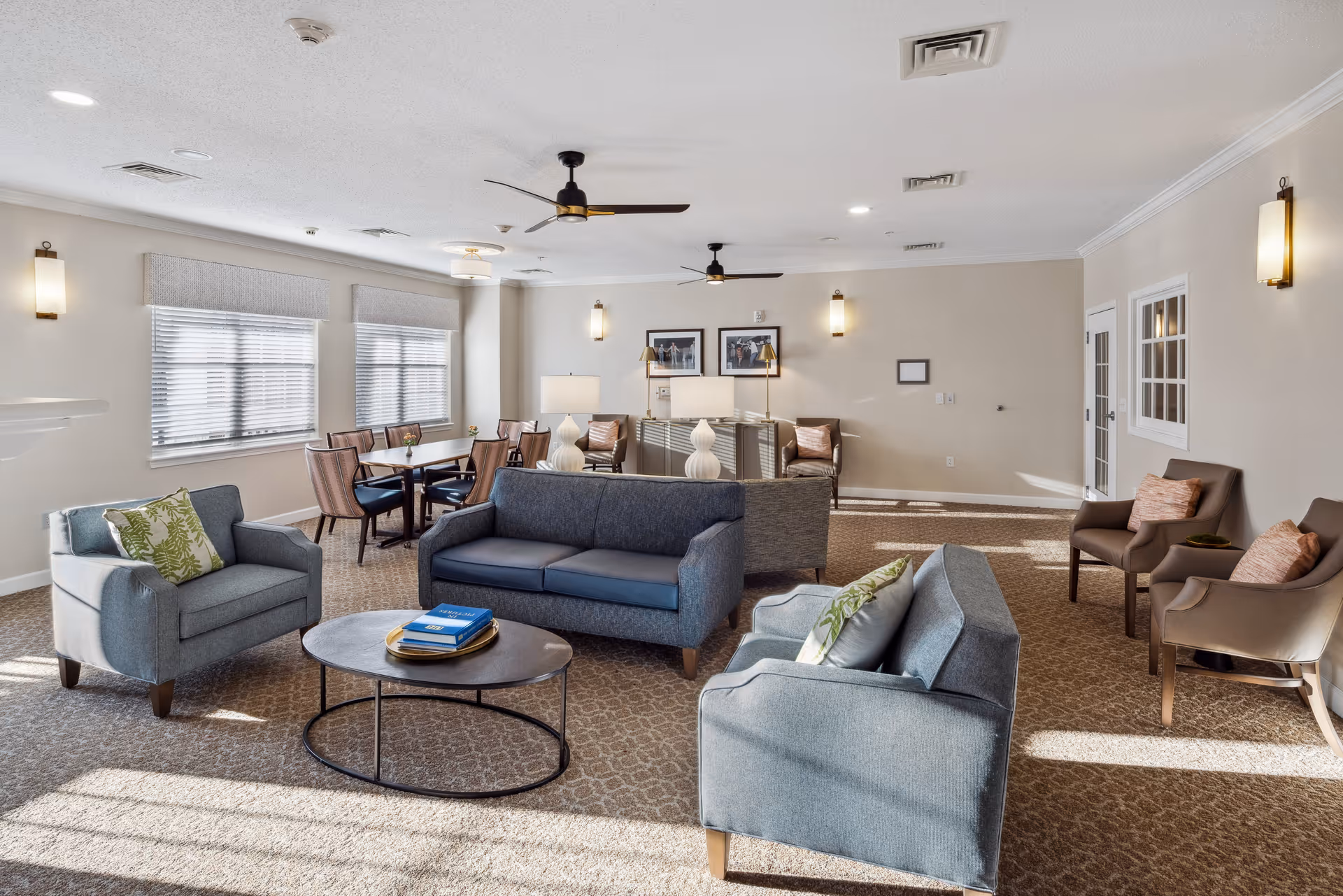 Bright communal living room with sofas, armchairs, a coffee table and a dining table in the background.