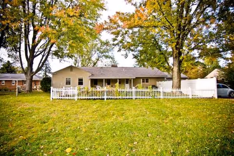 Single-story house with white picket fence, green lawn, and trees in front yard.