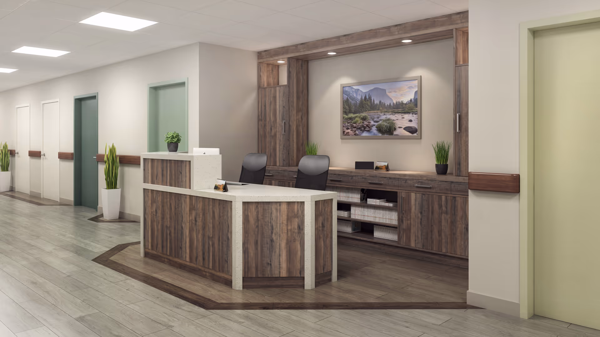 Reception area in a senior living facility with a wooden desk, two black chairs, potted plants, and a framed landscape painting on the wall behind the desk. The hallway has multiple doors and light-colored walls with wooden handrails.