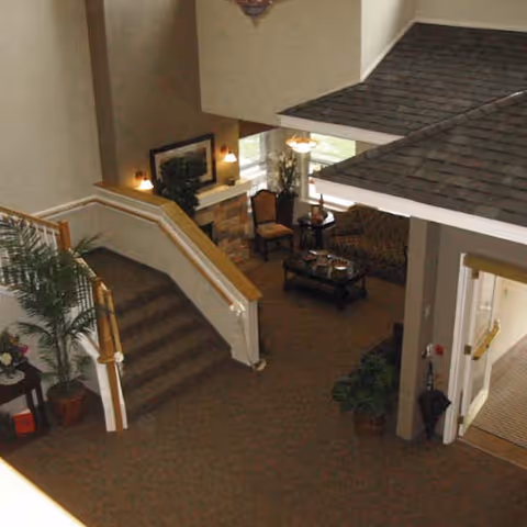 Interior lobby with a carpeted staircase, seating area with chairs and a coffee table, and a decorative indoor roof overhang.