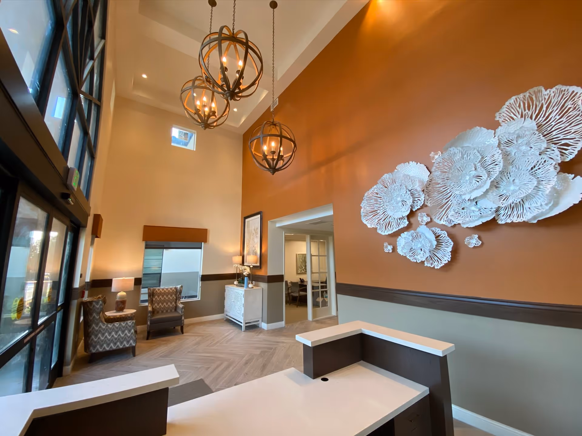 Lobby reception area with high ceilings, hanging chandeliers, seating, a front desk and large decorative wall art.