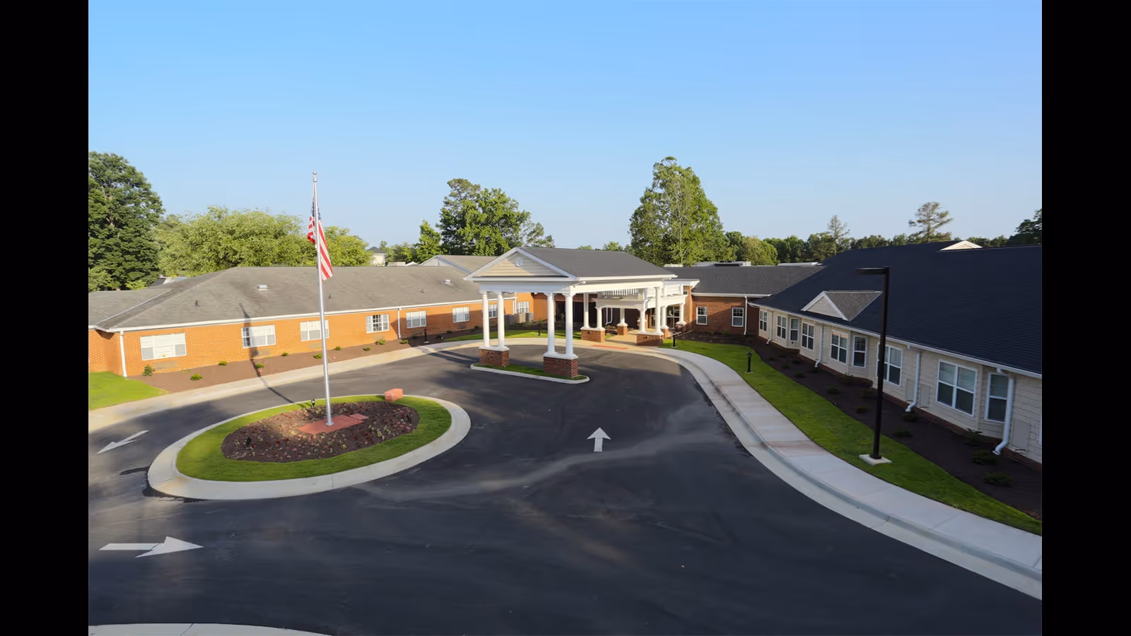 Entrance of a single-story senior living facility with a porte-cochère, circular driveway and flagpole.