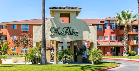 Exterior view of a senior living facility with palm trees and a welcoming entrance.