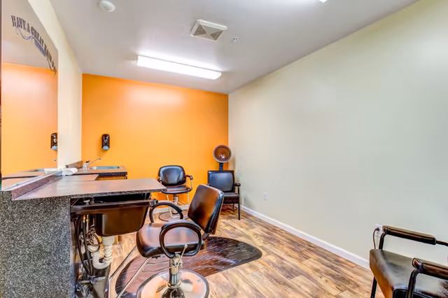Small salon room with styling chairs, shampoo sinks, mirrors and a hooded hair dryer against an orange accent wall.