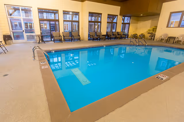 Indoor swimming pool with lounge chairs and large windows along the far wall.