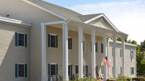 Exterior view of a beige senior living center with tall white columns and an American flag.