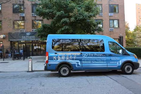 Blue Phoenix Rehabilitation and Nursing Center van parked in front of brick building entrance.
