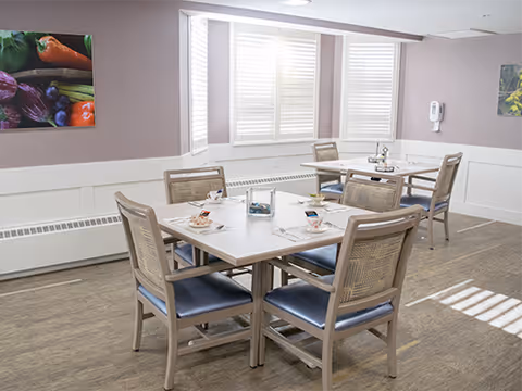 Small dining room with two square tables set for meals, wooden chairs, and shuttered windows.