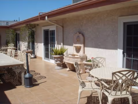 Sunlit outdoor patio with metal tables, chairs, and a wall fountain.