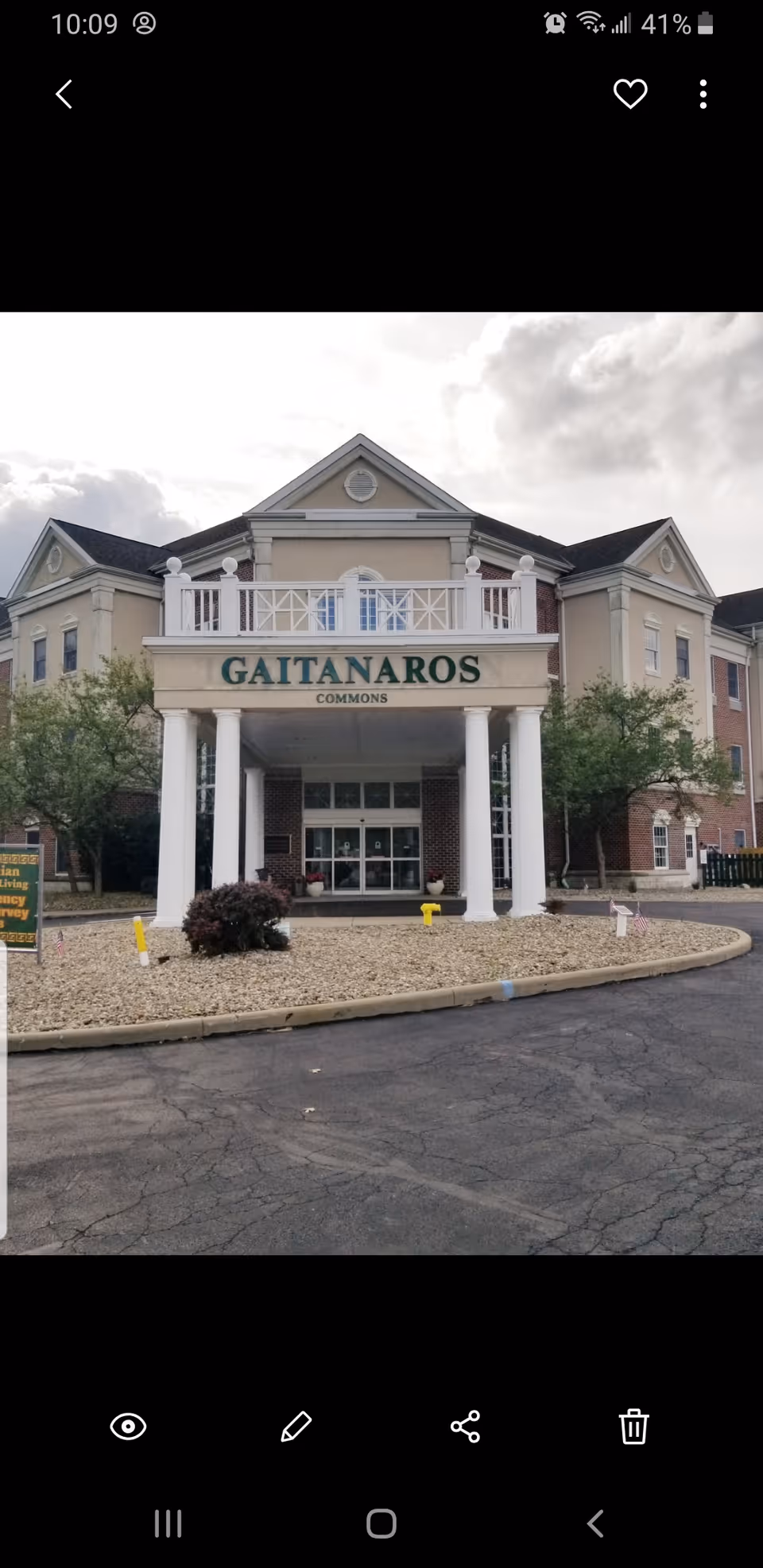 Front entrance of the Gaitanaros Commons building with white columns, a balcony, and a driveway in front.