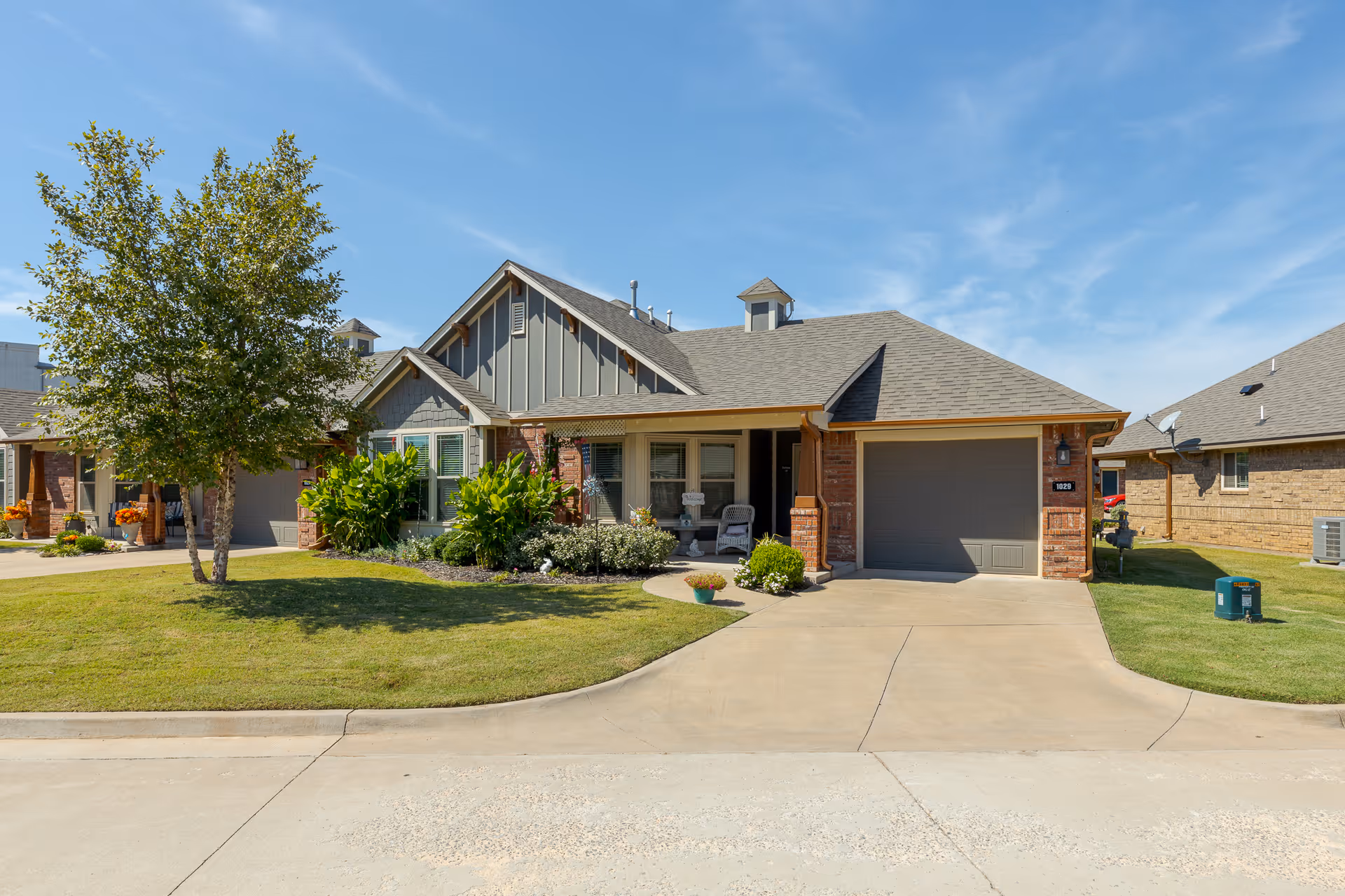 Single-story ranch-style house with an attached garage, front porch, driveway, lawn and tree under a clear blue sky.