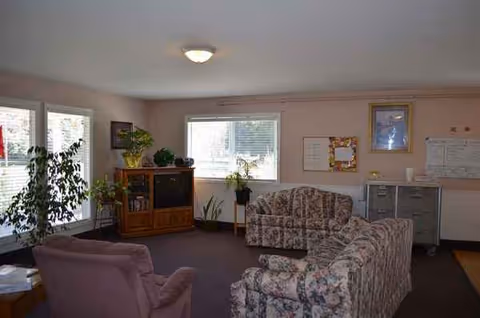 Cozy living room area with floral couches, a pink chair, plants, and cabinets.