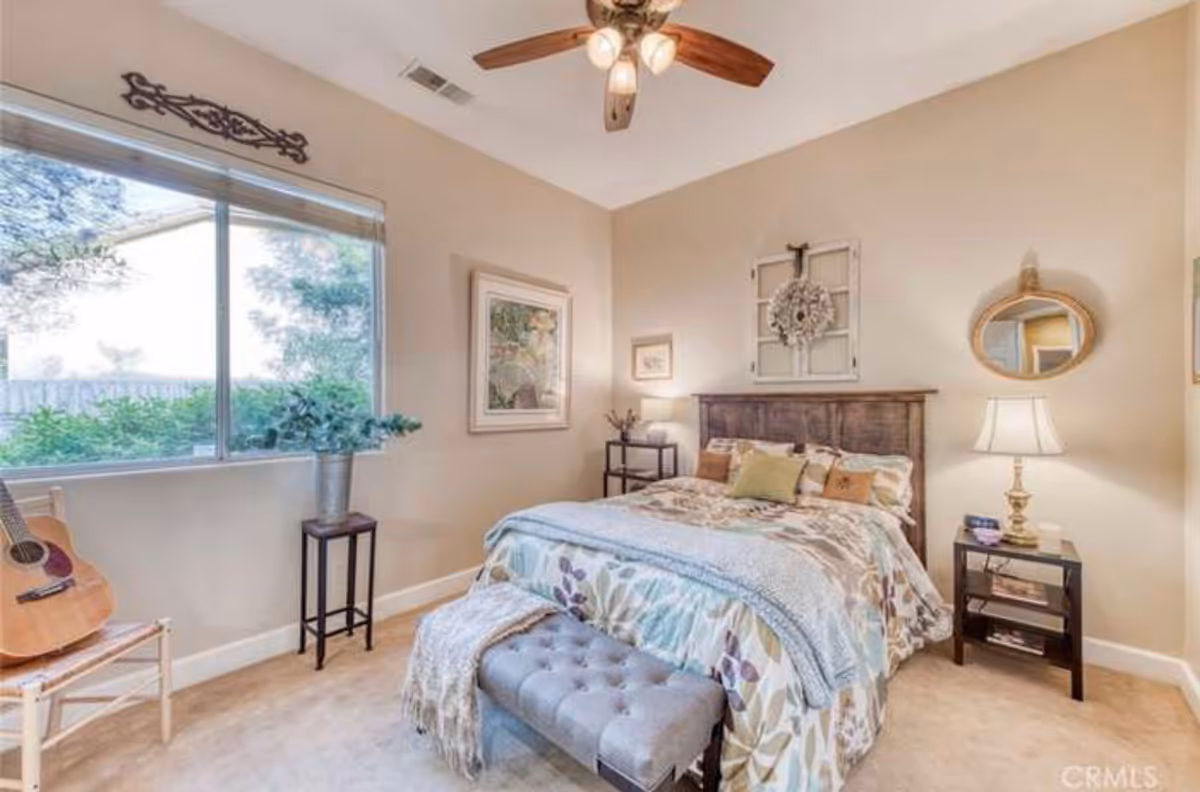 Furnished bedroom with a bed, nightstands, a large window, ceiling fan, and decorative accents.