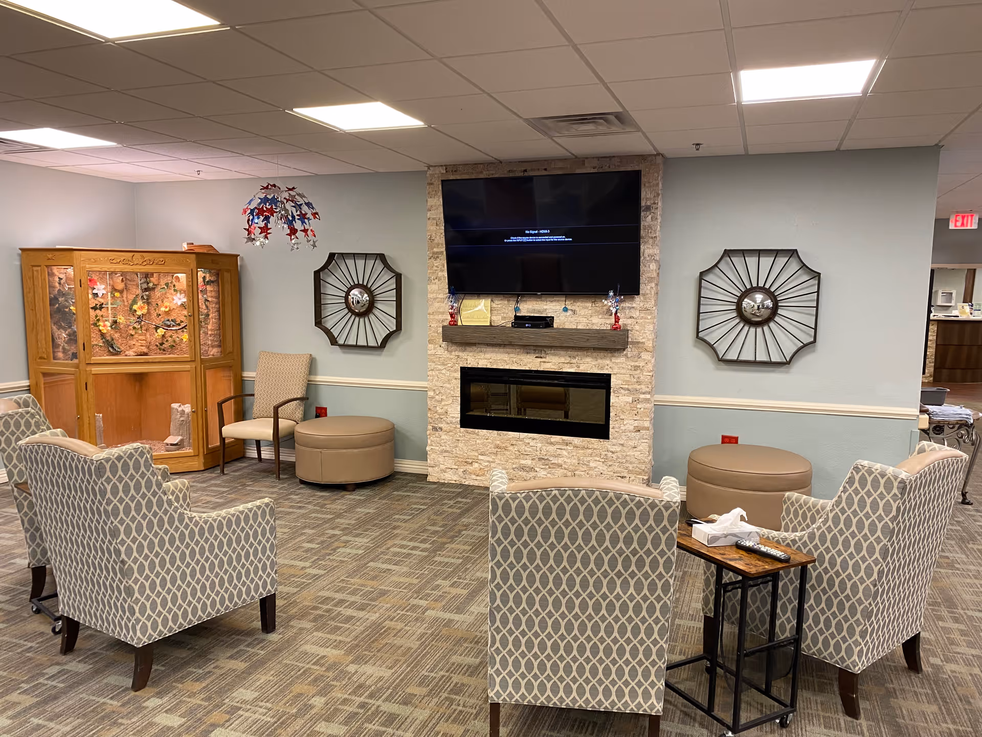 A cozy seating lounge with patterned armchairs arranged around a wall-mounted TV and electric fireplace.