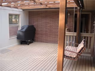 Covered outdoor patio with a grill, brick wall, and porch swing.