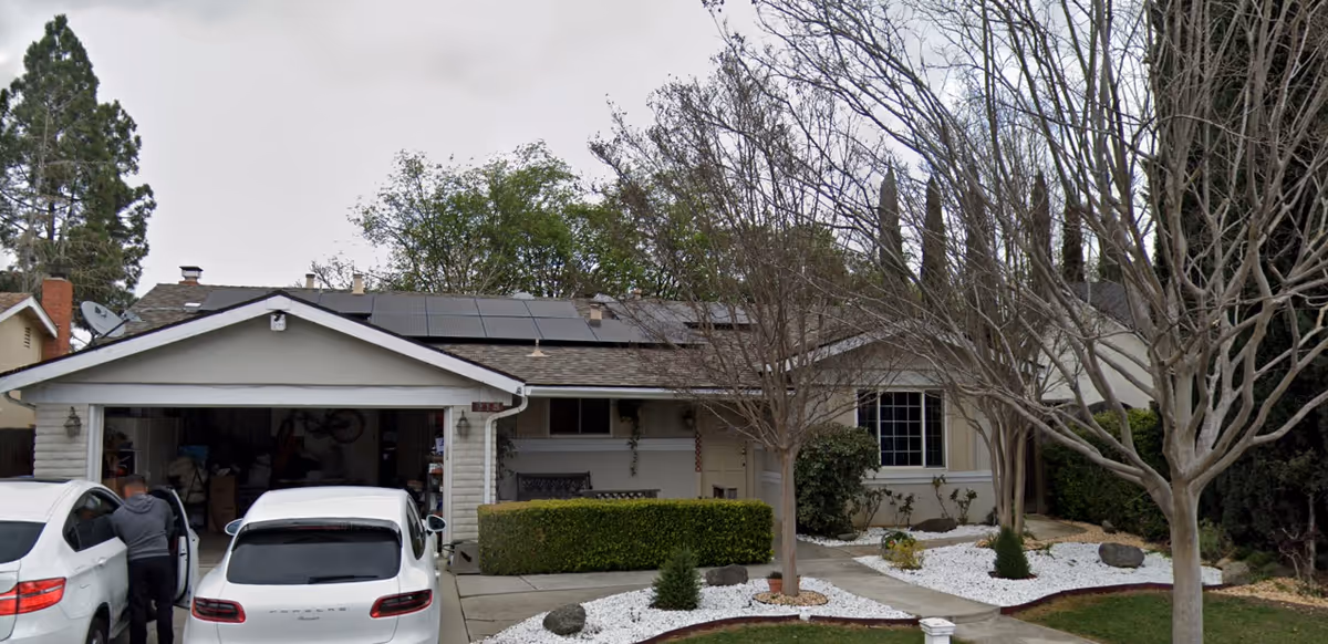 Front exterior view of a single-story house with a two-car garage, two white cars parked in the driveway, leafless trees, and a landscaped front yard with white rocks and shrubs.