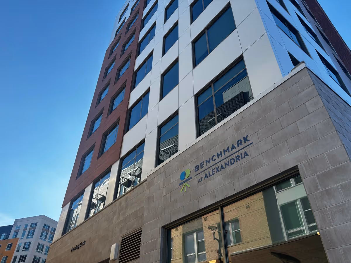 Street-level view of the exterior of a multi-story building with a 'Benchmark at Alexandria' sign.