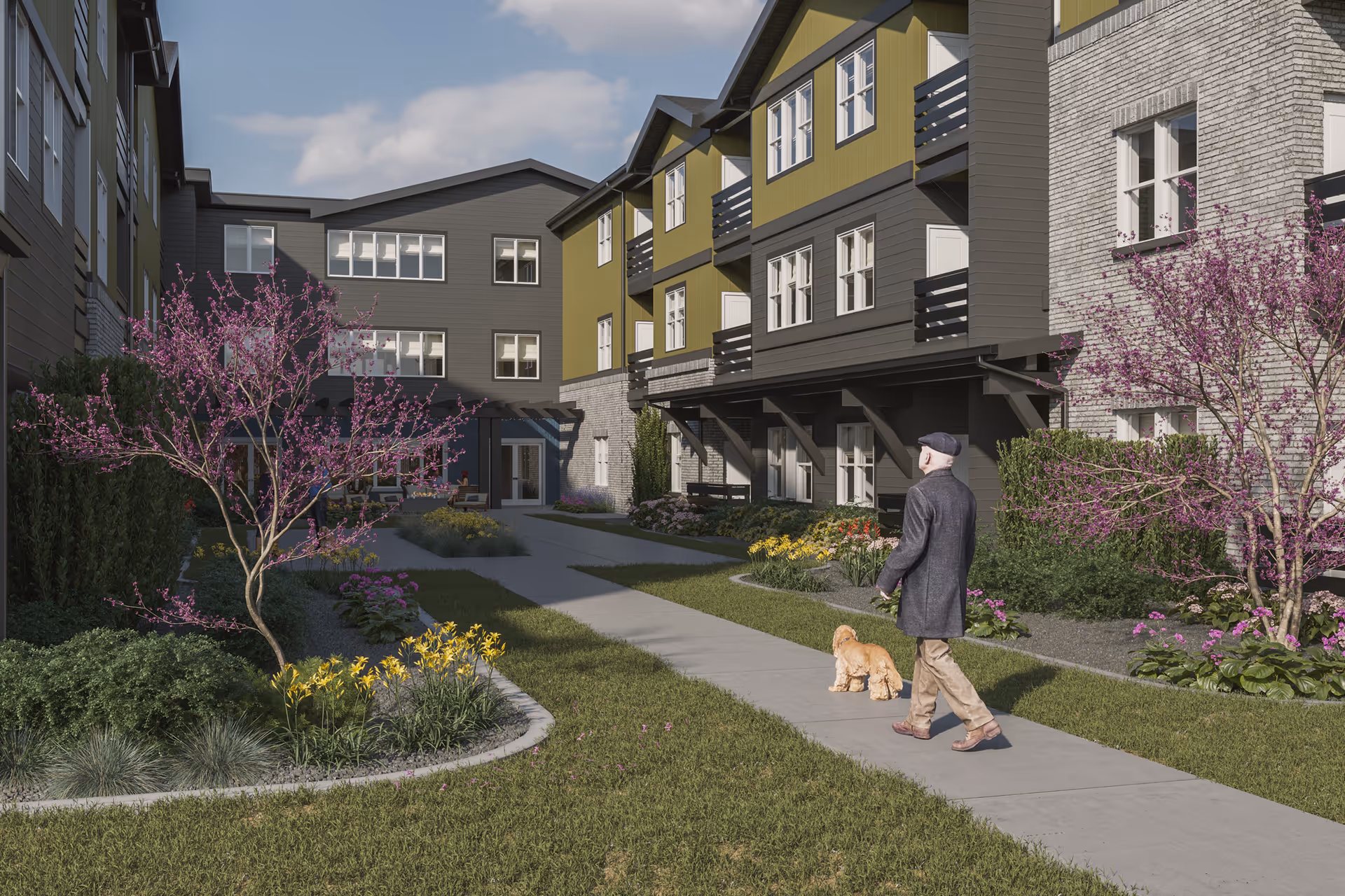 An elderly man walking a small dog on a paved pathway through a landscaped courtyard of a senior living facility. The courtyard is surrounded by multi-story buildings with a mix of gray and olive green siding and brick accents. Flowering trees and colorful flower beds line the pathway under a partly cloudy sky.