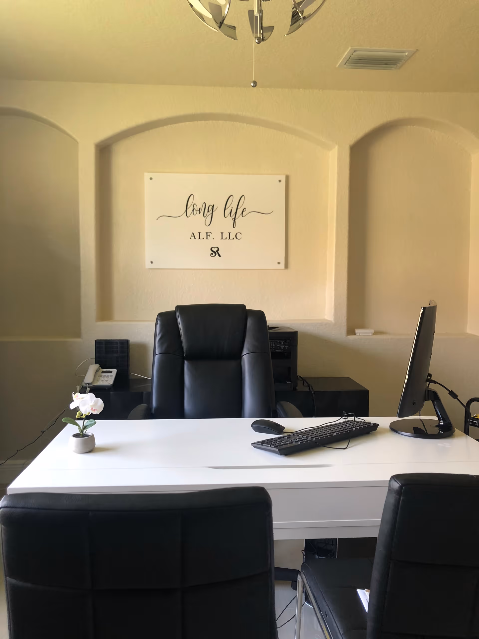 Reception-style office with a white desk, black leather chairs, a computer monitor and a wall sign that reads 'long life ALF, LLC'.
