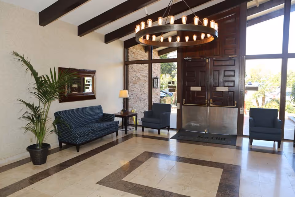 Lobby of Sea Cliff Assisted Living with chairs, a sofa, a potted plant, a chandelier, and double front doors.