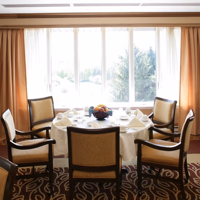 Round dining table with place settings and fruit centerpiece in a bright dining room.