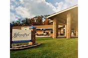 Exterior view of Jefferson Park at Dandridge senior living facility with a brick entrance sign and a covered driveway entrance under a partly cloudy sky.