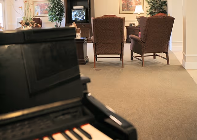 Blurred piano keys in the foreground with upholstered armchairs and a television in a communal lounge.